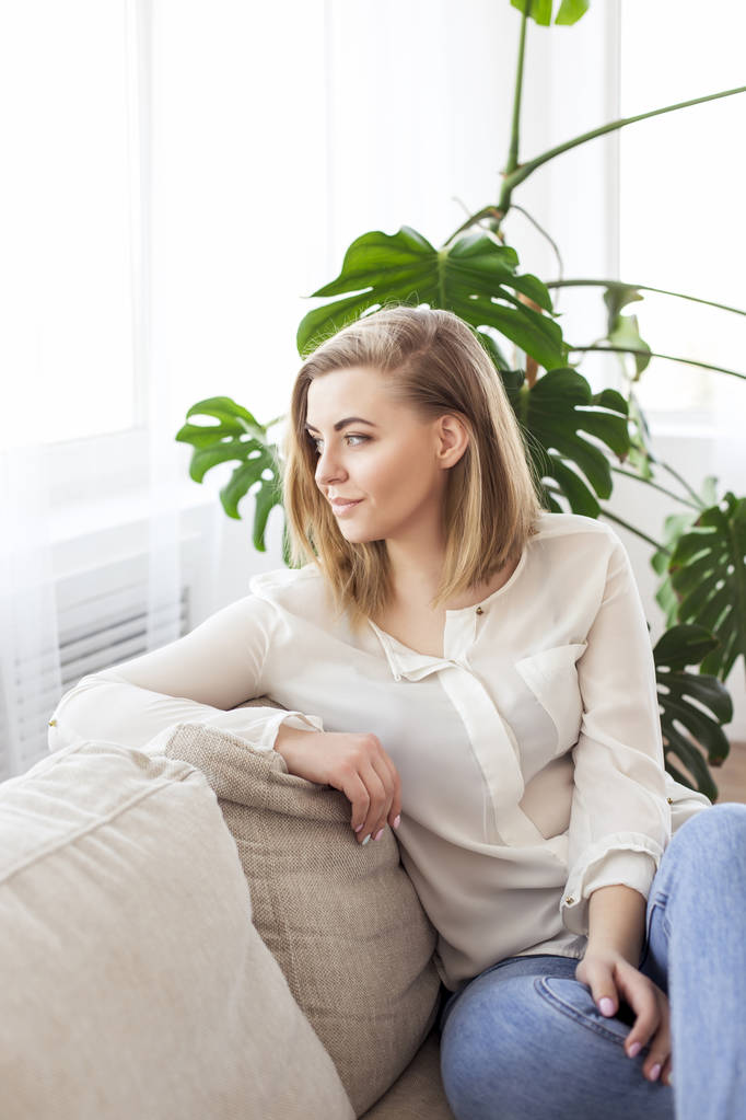 Atractiva joven con una camisa blanca está sentada en un apartamento en el sofá
 - Foto, imagen