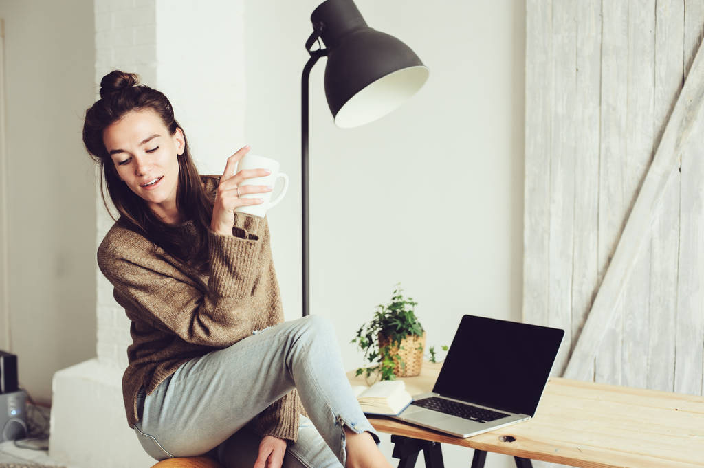 mladé krásné blogger žena doma online nakupování s notebookem a šálku kávy v dopoledních hodinách. Domácí kancelář v moderním skandinávském interiéru - Fotografie, Obrázek