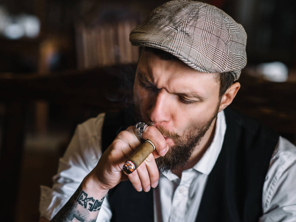 Ένας νεαρός γενειοφόρος άνδρας καπνίζοντας ένα πούρο σε μια παμπ - Φωτογραφία, εικόνα