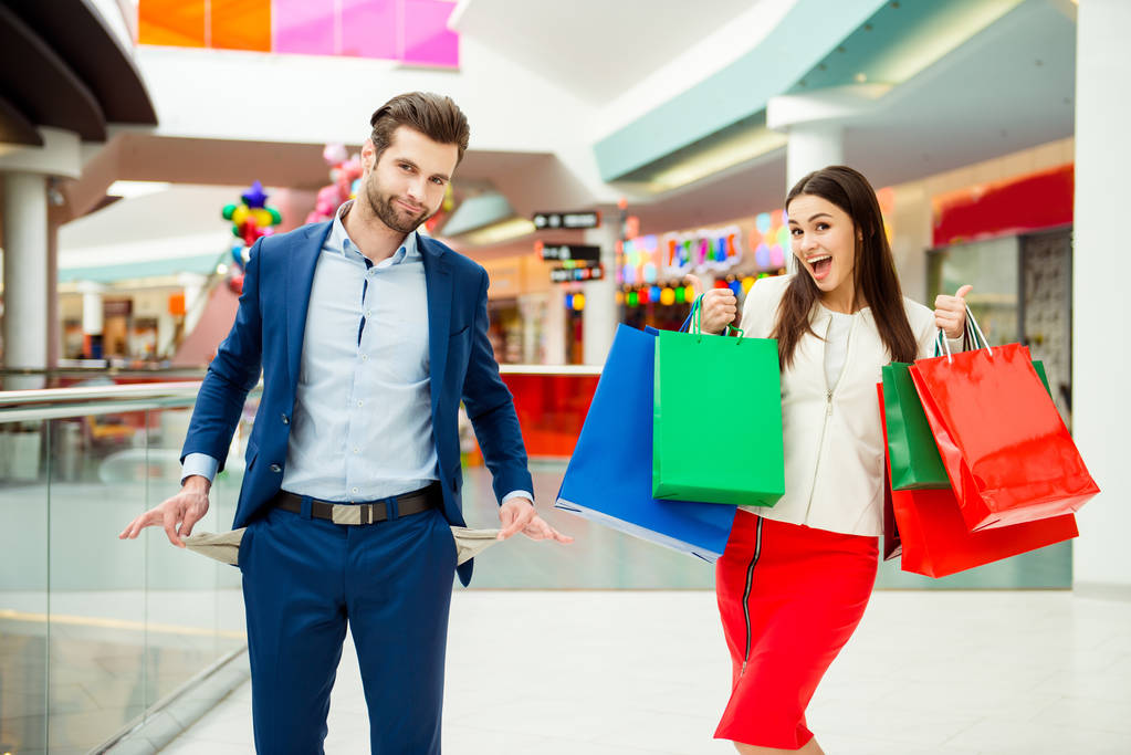 To je nakupování čas s prodejem a zábavy. Roztomilý veselý úspěšné šťastný krásný pár v bundě drží barevné nákupní tašky, odkazující na obchod a směje se v obchoďáku na dovolené - Fotografie, Obrázek