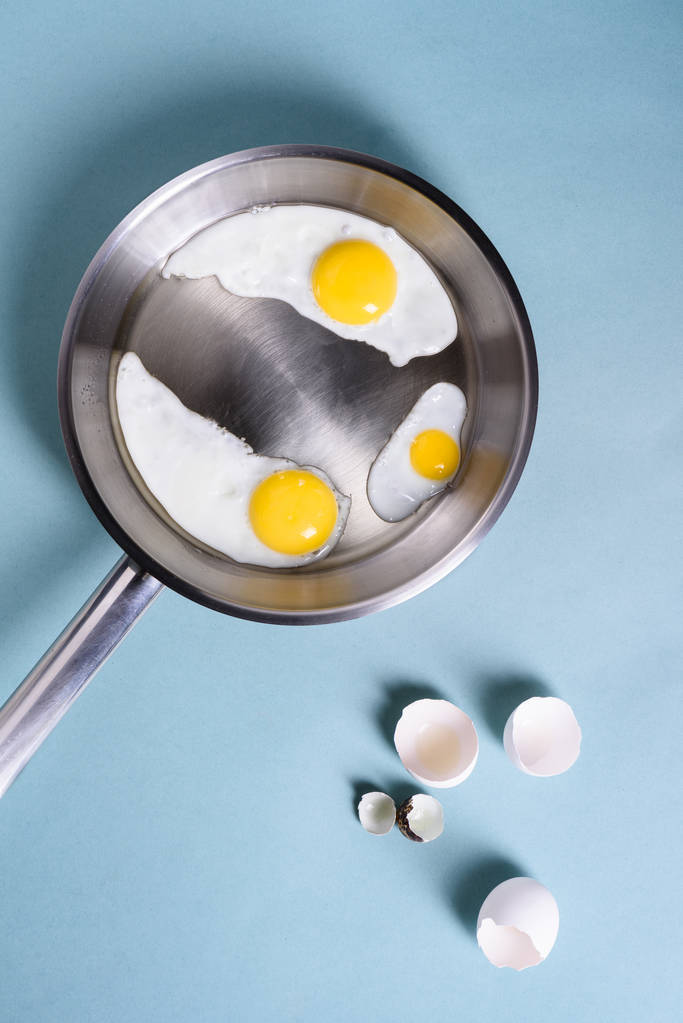 Жареные яйца на завтрак в кастрюле. Куриное яйцо, перепелиное яйцо, желток и яичная скорлупа. Вид сверху
,  - Фото, изображение