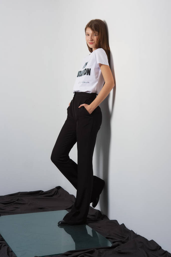 Atractiva modelo de moda en pantalones y camiseta con estampado apoyado en la pared
 - Foto, Imagen