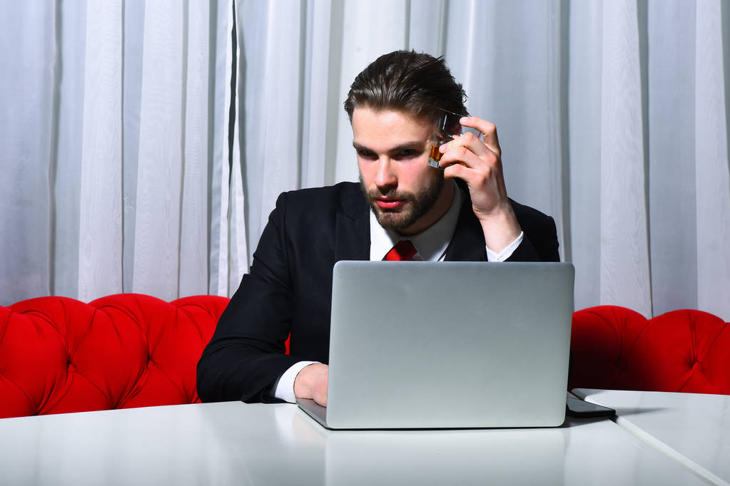 homme barbu, homme d'affaires tenant un verre de whisky travaille à l'ordinateur portable - Photo, image
