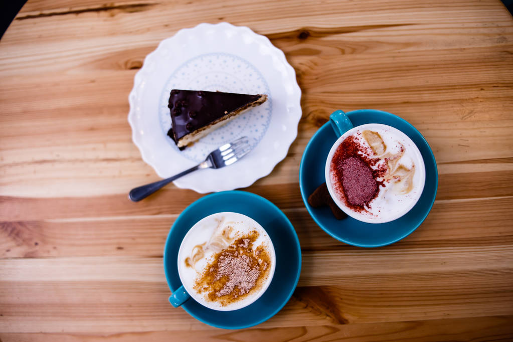 Δύο φλιτζάνια καφέ με κανέλα είναι στο τραπέζι με ένα κομμάτι κέικ σοκολάτας - Φωτογραφία, εικόνα