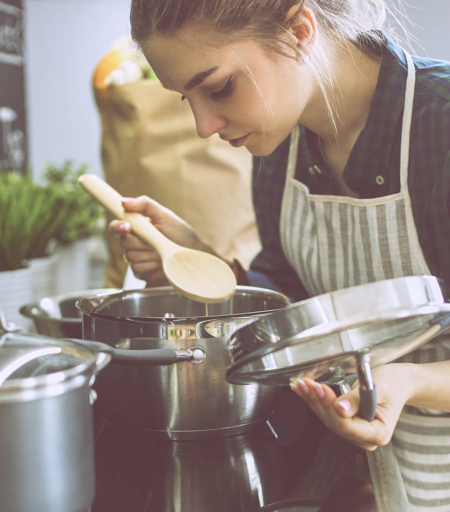 Jeune femme cuisine dans sa cuisine debout près de la cuisinière - Photo, image