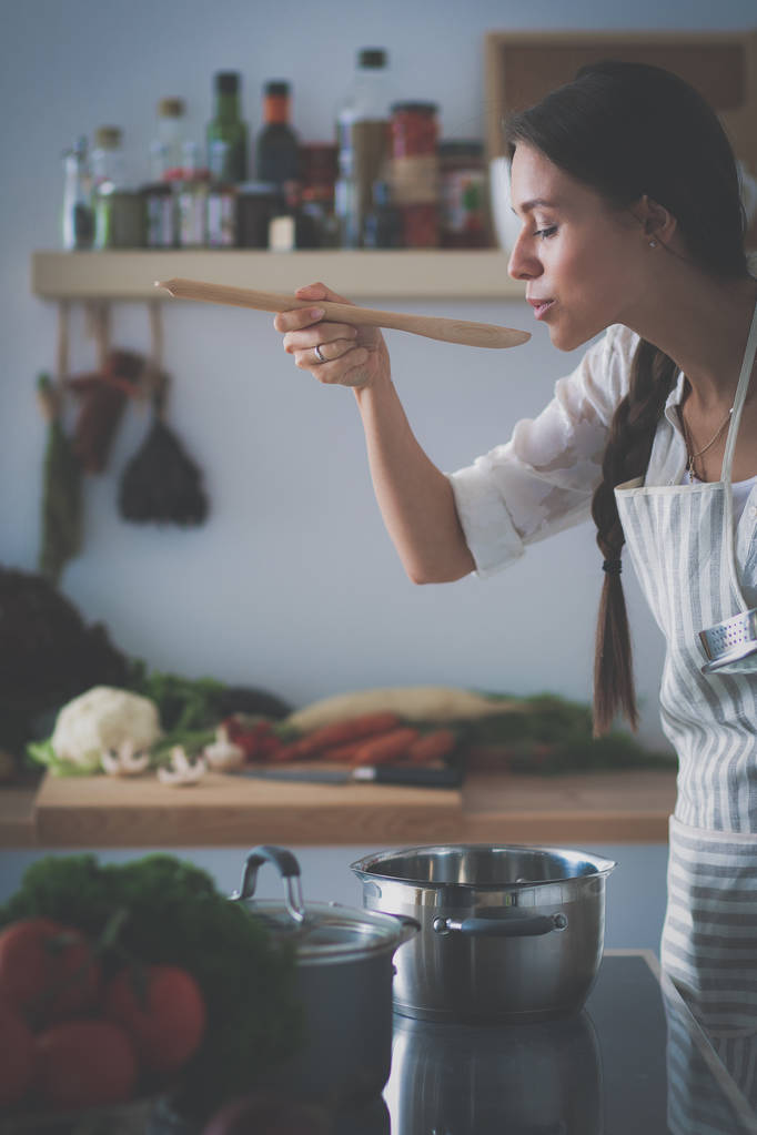 Mutfakta ahşap kaşıkla yemek pişiren kadın - Fotoğraf, Görsel