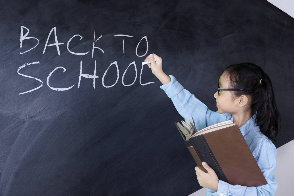 Schoolgirl writing back to school word on chalkboard  - Photo, Image