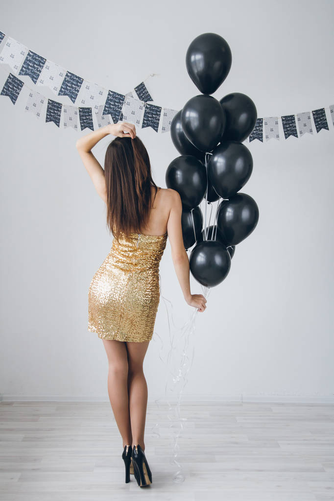 Chica en un vestido de oro con globos negros
 - Foto, imagen