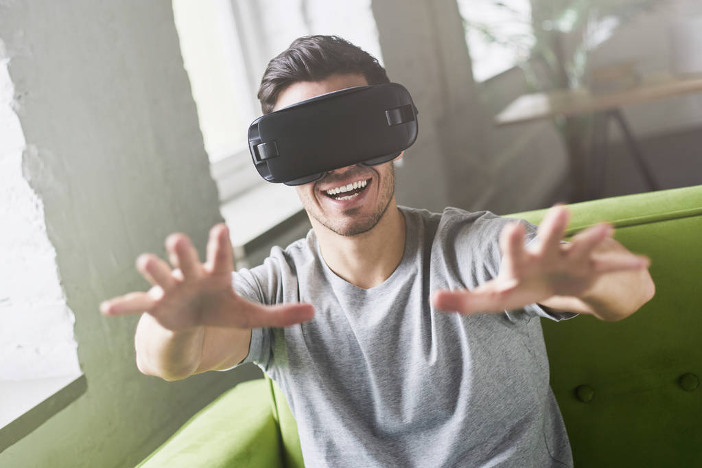 Nahaufnahme Porträt eines verblüfften gutaussehenden Kerls, der Virtual Reality erlebt, während er das Oculus Rift Headset zur Unterhaltung benutzt, zu Hause auf der Couch sitzend. Menschen, Technologie und Innovationskonzept - Foto, Bild