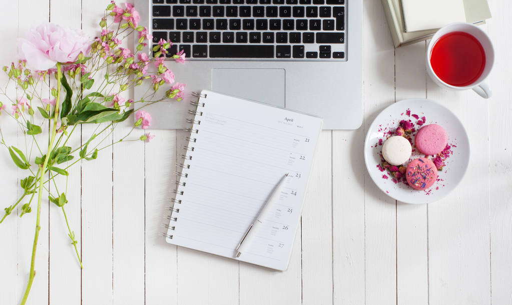 Vrouwelijke flat leg werkruimte met laptop, kopje thee, macarons en bloemen op witte houten tafel. Bovenaanzicht mock up. - Foto, afbeelding
