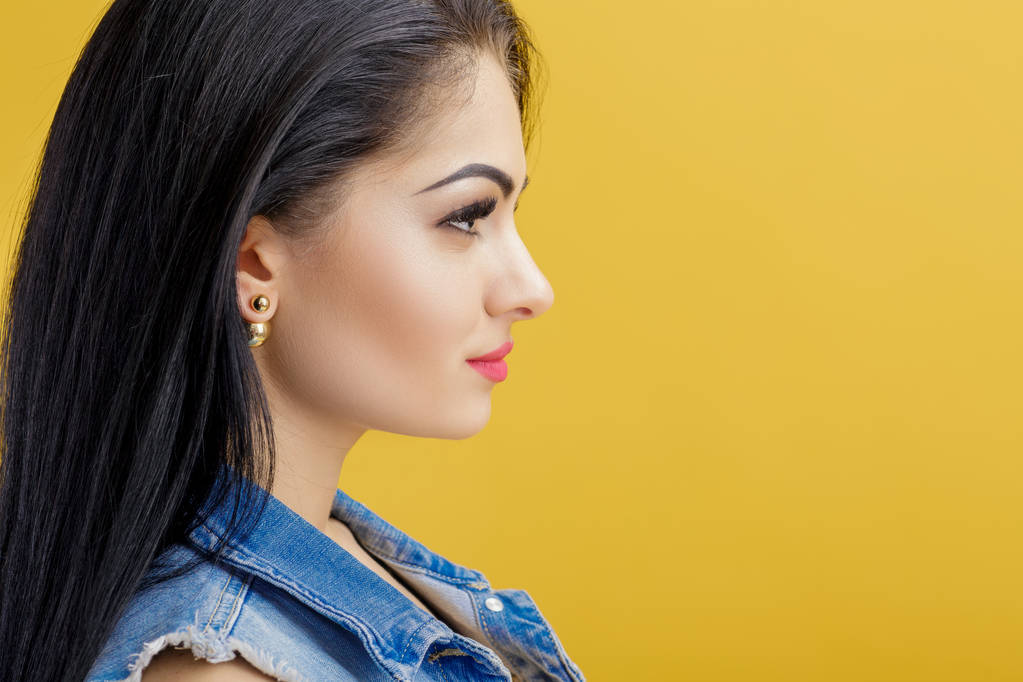 portret atrakcyjna młoda kobieta brunetka w drelichu kamizelki na żółtym tle. - Zdjęcie, obraz