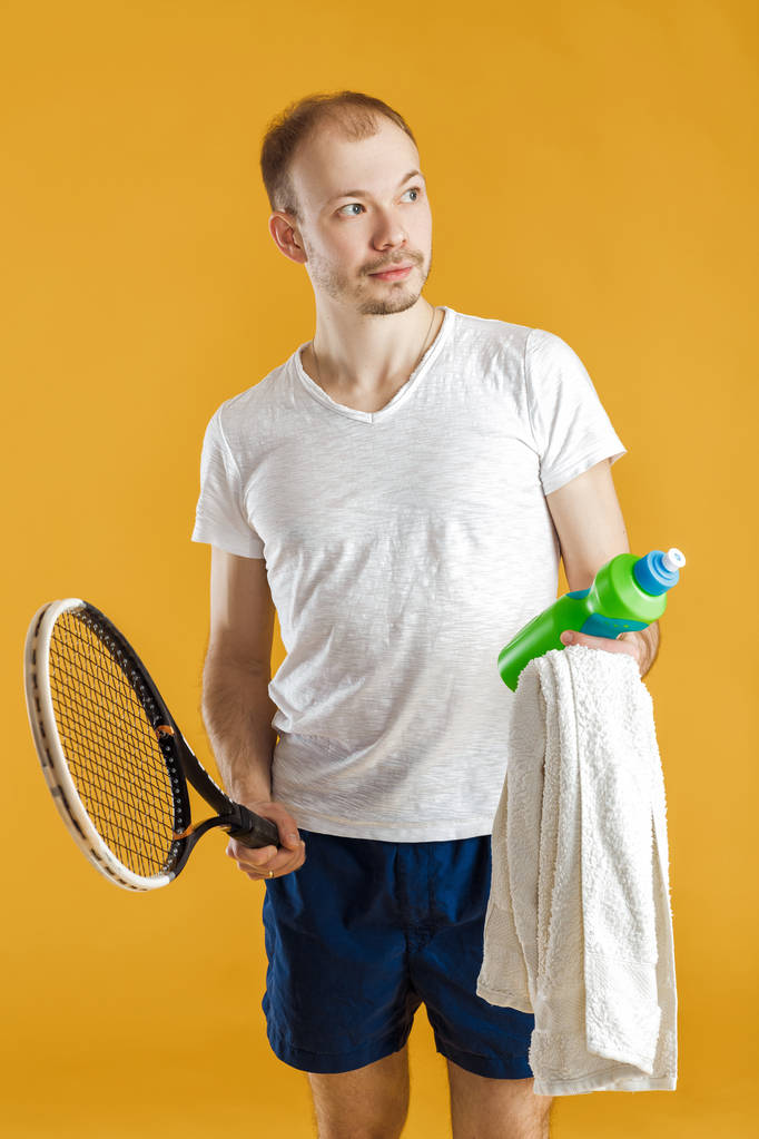 молодий тенісист з рушником тримає тенісну ракетку на жовтому фоні
 - Фото, зображення