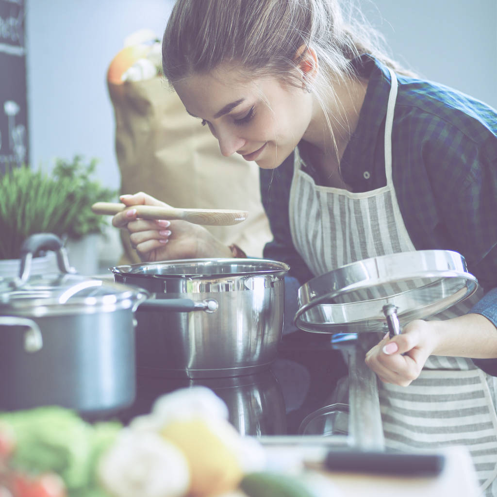 Mladá žena, vaření ve své kuchyni stojí poblíž sporáku - Fotografie, Obrázek