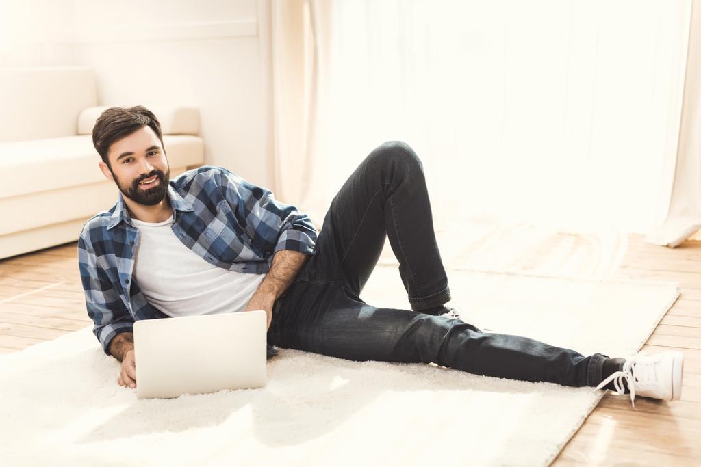 Mann liegt auf Teppich und benutzt Laptop - Foto, Bild