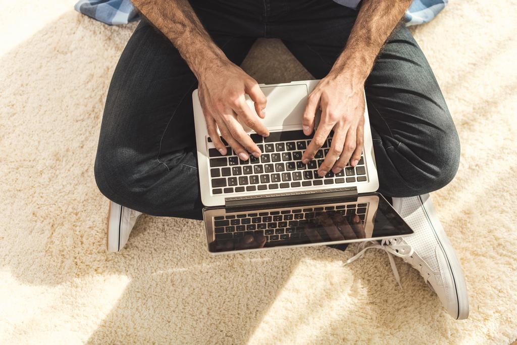 Hombre sentado en la alfombra y escribiendo en el ordenador portátil
 - Foto, imagen