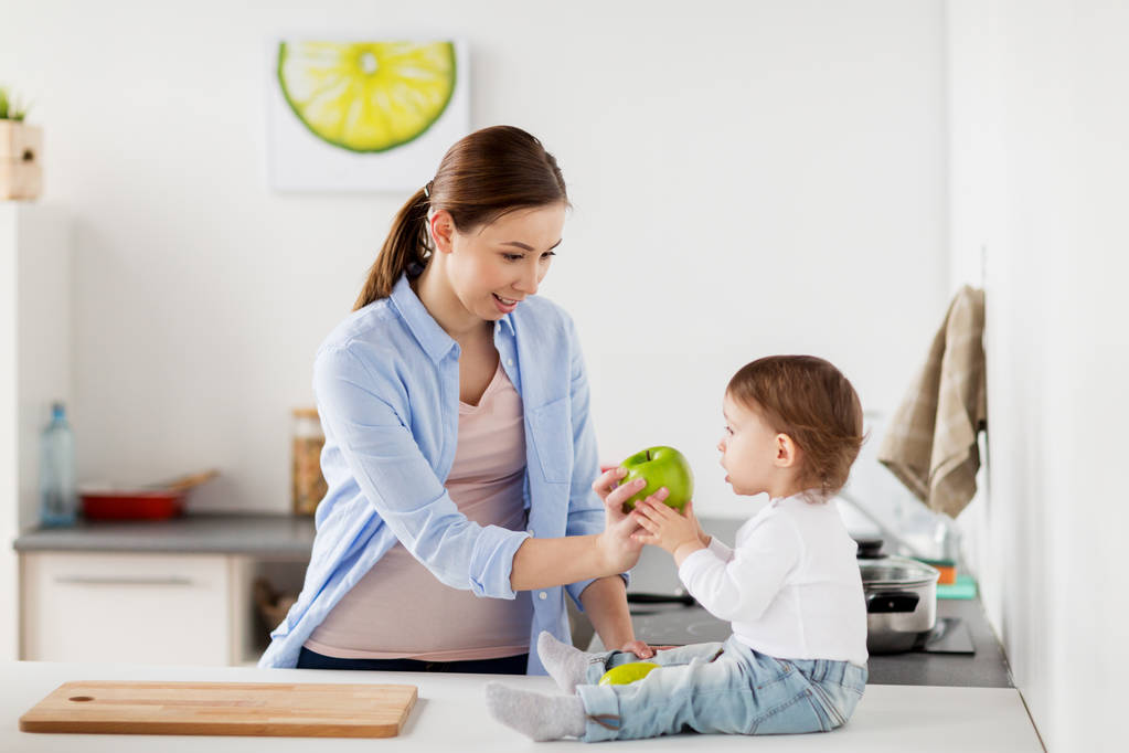 мать дает зеленое яблоко ребенку на домашней кухне
 - Фото, изображение