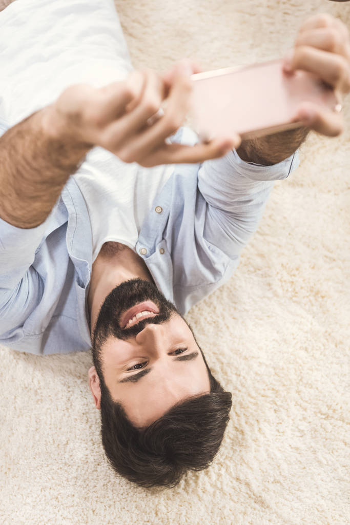 мужчина делает селфи, лежа на ковре
 - Фото, изображение