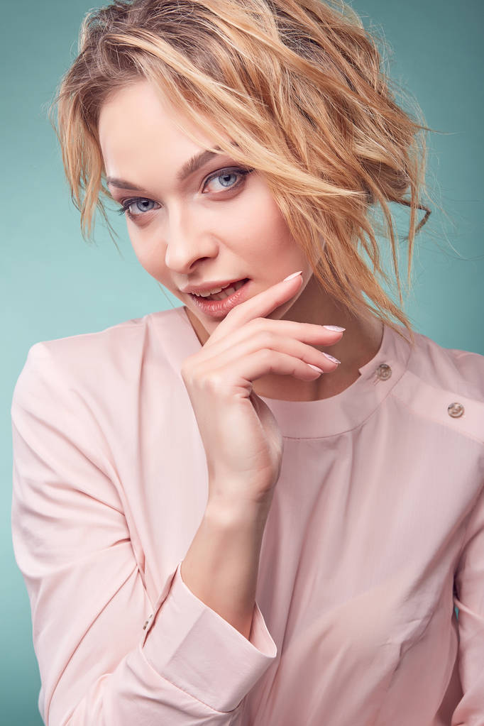 Retrato de joven mujer rubia romántica seria con ojos grandes y cabello ondulado, sonrisa sexy, vestido rosa claro en el estudio sobre fondo turquesa claro
 - Foto, imagen