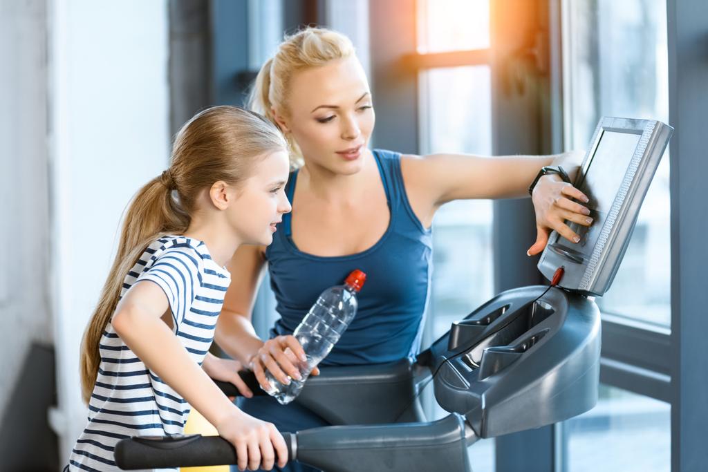 Vrouw trainer met klein meisje workout op een loopband - Foto, afbeelding
