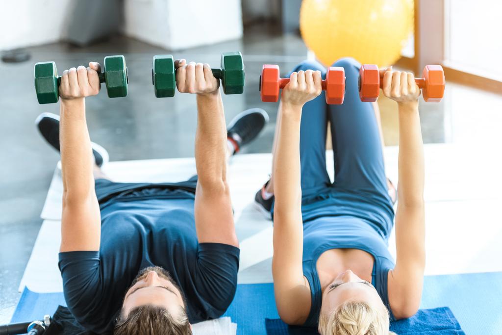 Un par de jóvenes de fitness haciendo ejercicio con pesas en el gimnasio
 - Foto, Imagen