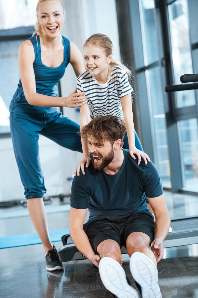 Woman with girl embrace tired father sitting on treadmill at gym - Photo, Image