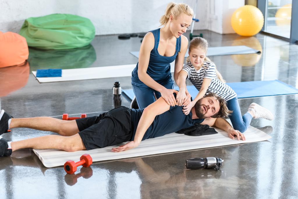 Woman with girl helping tired man lying on mat at gym - Photo, Image