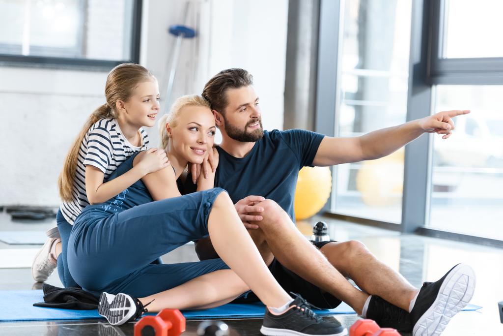 Porträt einer glücklichen Familie, die im Fitnessstudio auf Matten sitzt - Foto, Bild
