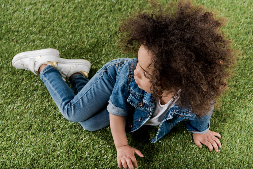 Lockiges Mädchen ruht sich auf Rasen aus - Foto, Bild