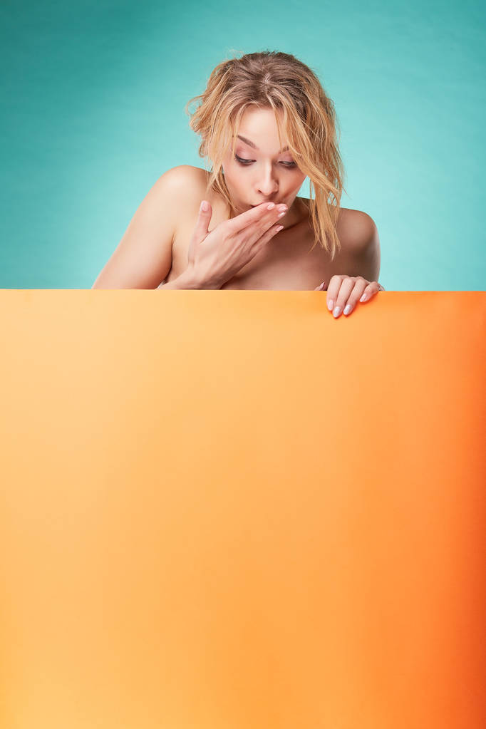 Giovane donna bionda sorpresa in posa in studio con sfondo turchese e foglio arancione
 - Foto, immagini