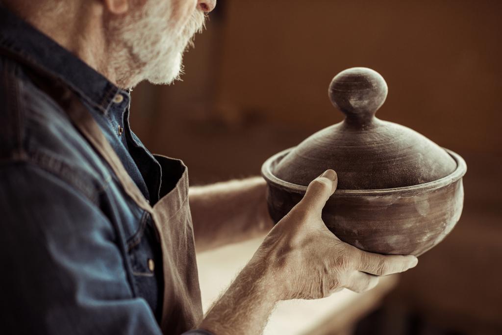Starszy potter w fartuch, badając miski ceramiczne o warsztatów - Zdjęcie, obraz