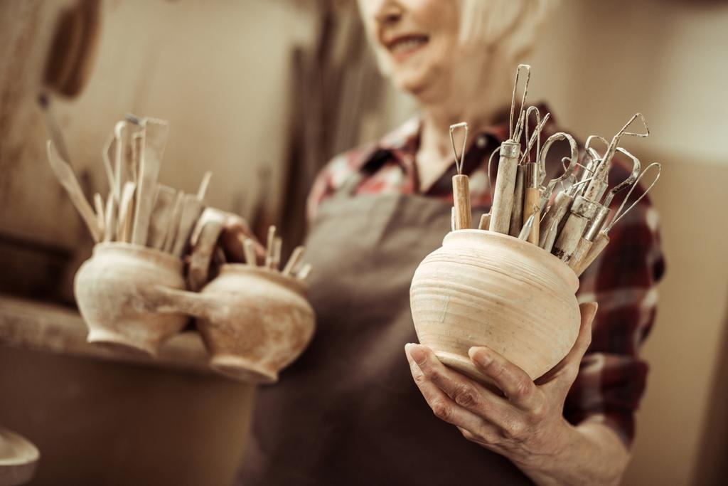 ワーク ショップで鉢で陶器のツールを保持している年配の女性 - 写真・画像