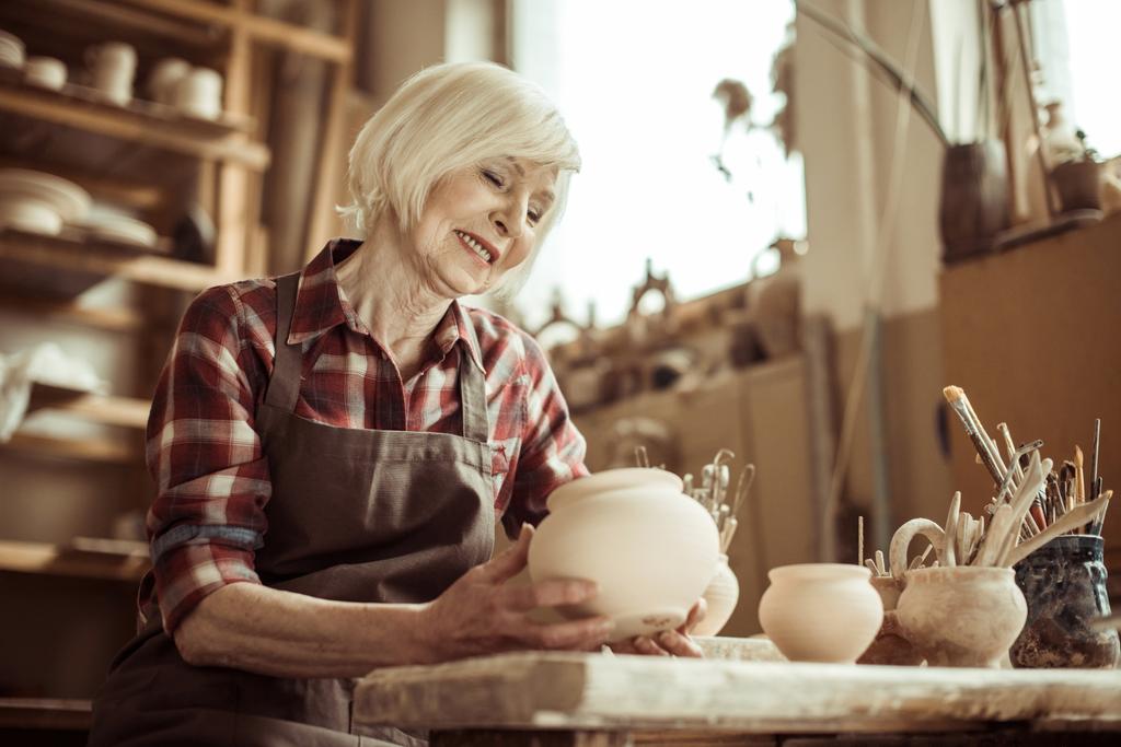 Женщина-гончар сидит за столом и рассматривает керамическую миску в мастерской
 - Фото, изображение