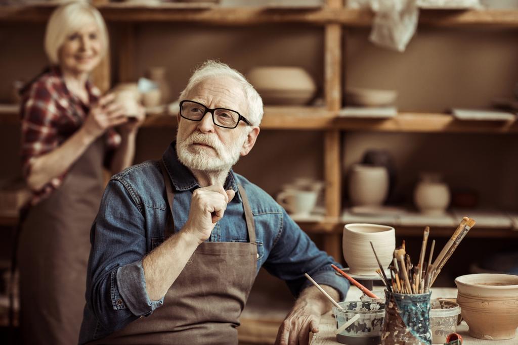 Ceramista anziano seduto a tavola e pensare con la donna anziana in officina
 - Foto, immagini