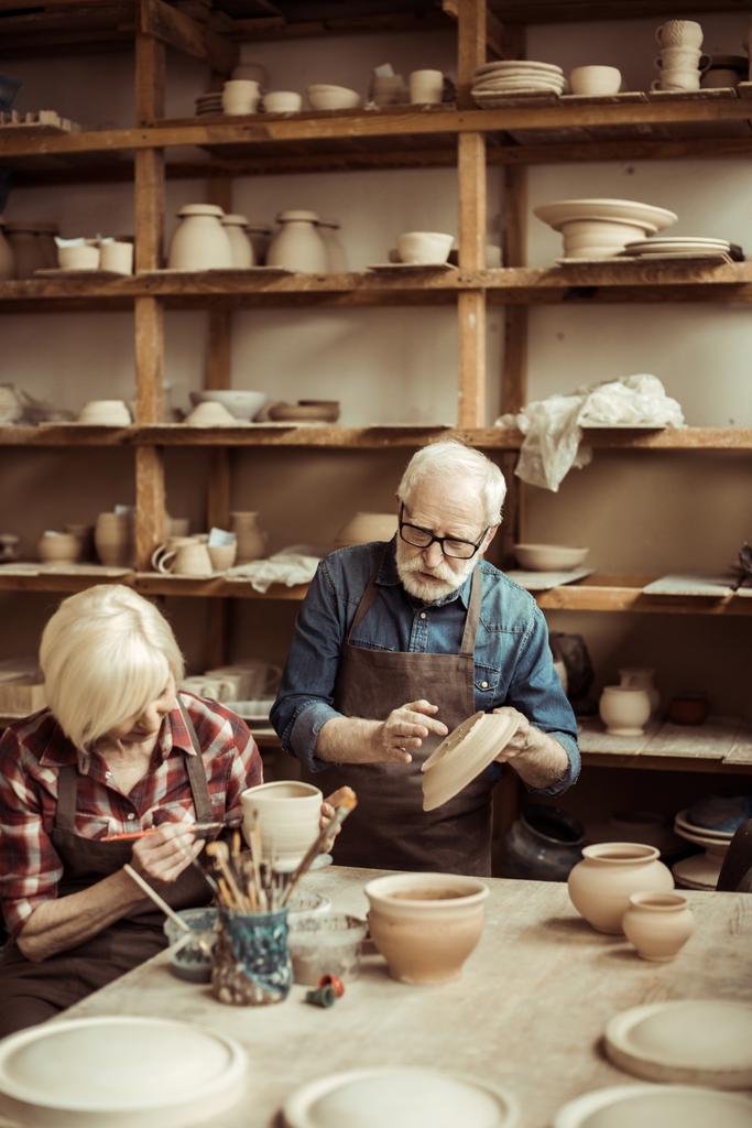 Жінка малює глиняний горщик з старшим гончарним в майстерні
 - Фото, зображення