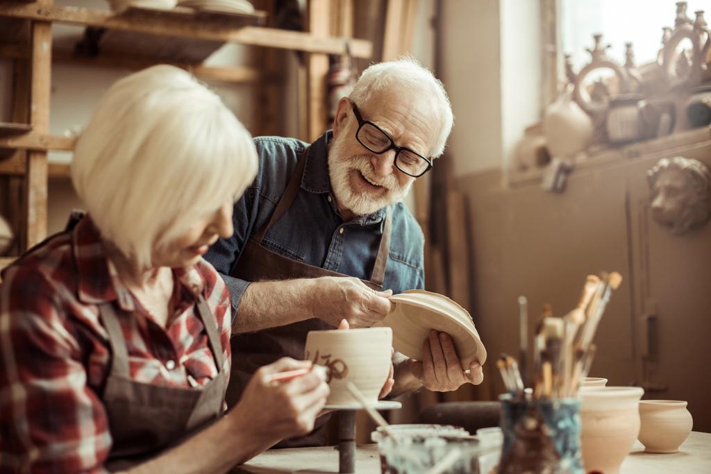 Жінка малює глиняний горщик з старшим гончарним в майстерні
 - Фото, зображення