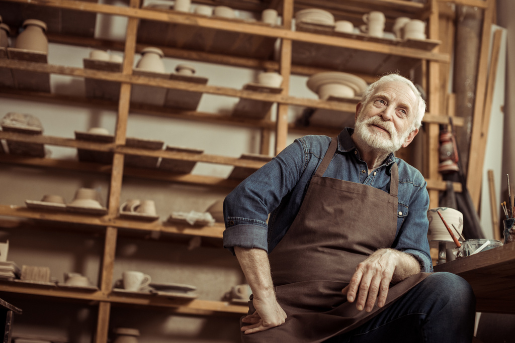 Старший гончар в фартуке сидит за столом и мечтает о производстве
 - Фото, изображение