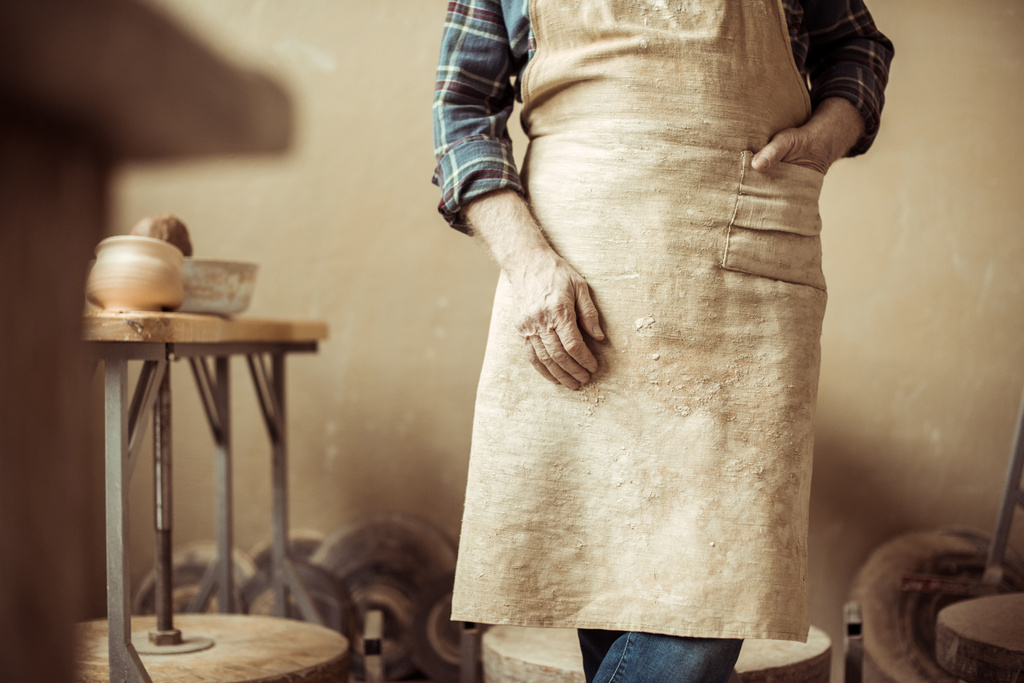 Imagen recortada de alfarero senior en delantal de pie en el taller
 - Foto, Imagen