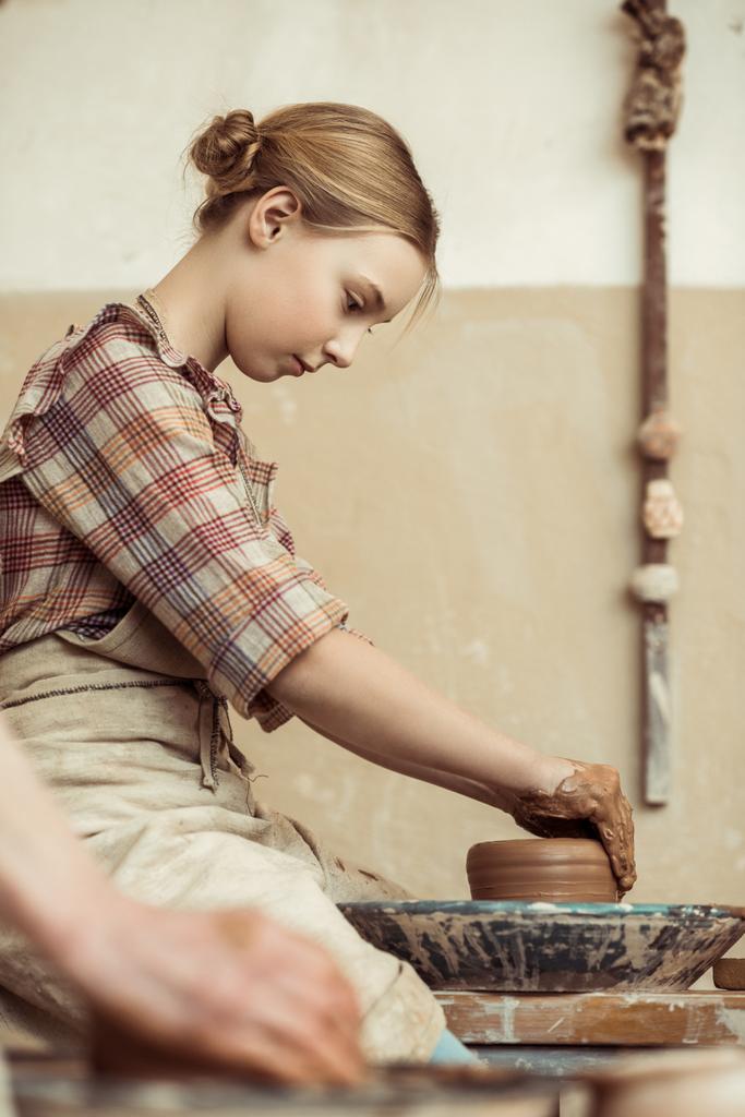 Vue latérale de la petite fille faisant de la poterie sur roue à l'atelier
 - Photo, image