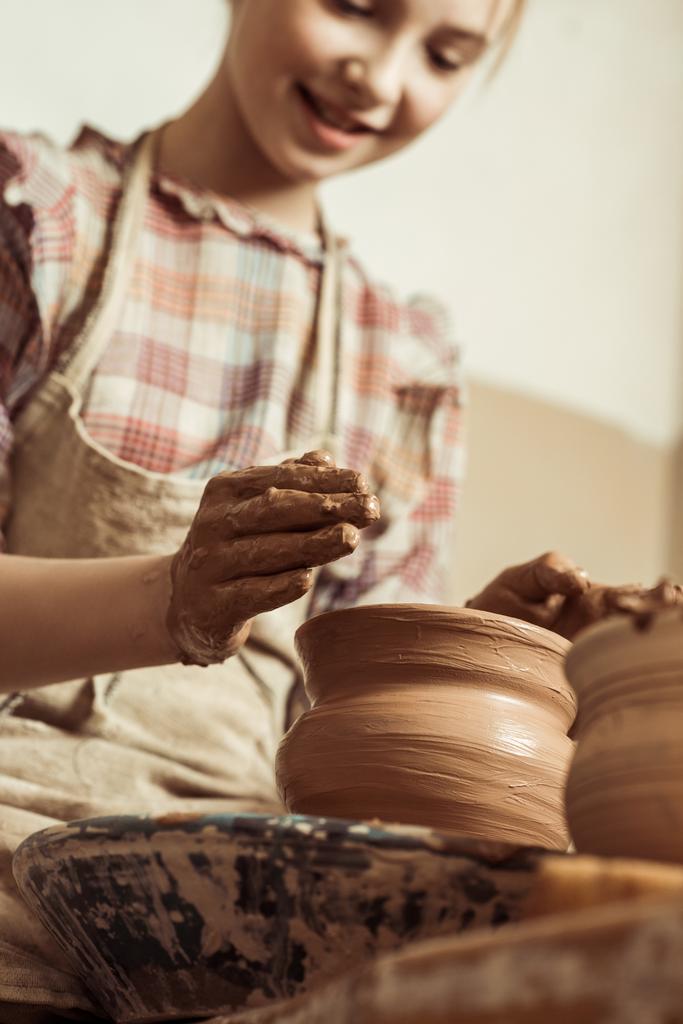 Крупный план маленькой девочки, делающей керамику на колесах в мастерской
 - Фото, изображение