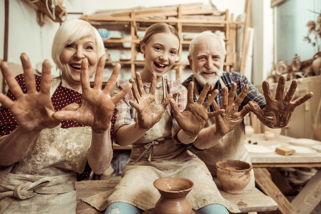 Abuela y abuelo con nieta mostrando las manos en arcilla en el taller
 - Foto, Imagen