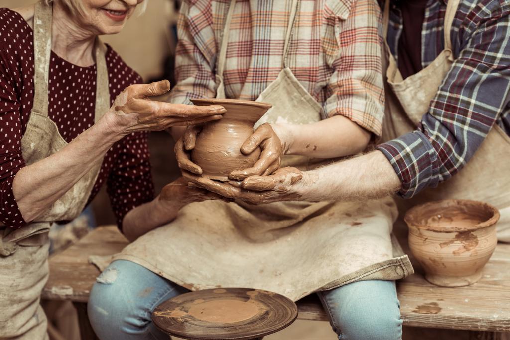 Обрезанное изображение бабушки и дедушки с внучкой, делающей керамику в мастерской
 - Фото, изображение