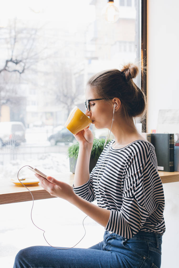 Tyttö kuuntelee musiikkia älypuhelimeen ja juo kahvia
 - Valokuva, kuva