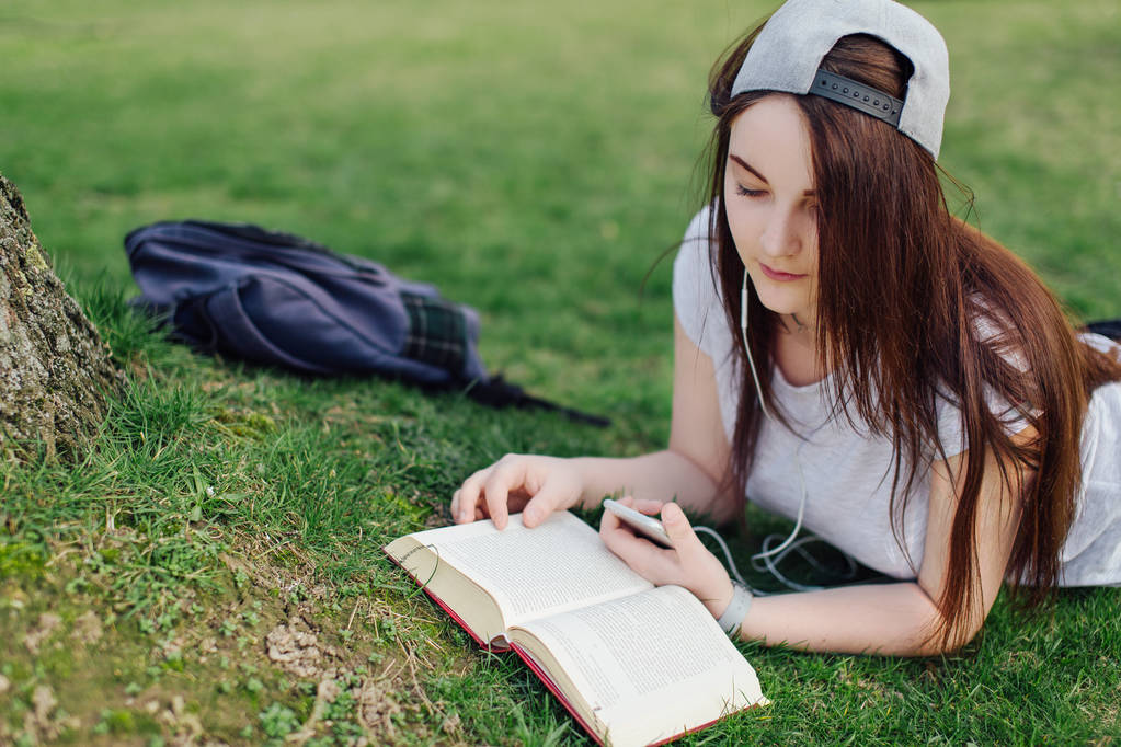 Kaunis tyttö lukea kirjaa ja kuunnella musiikkia puistossa
 - Valokuva, kuva