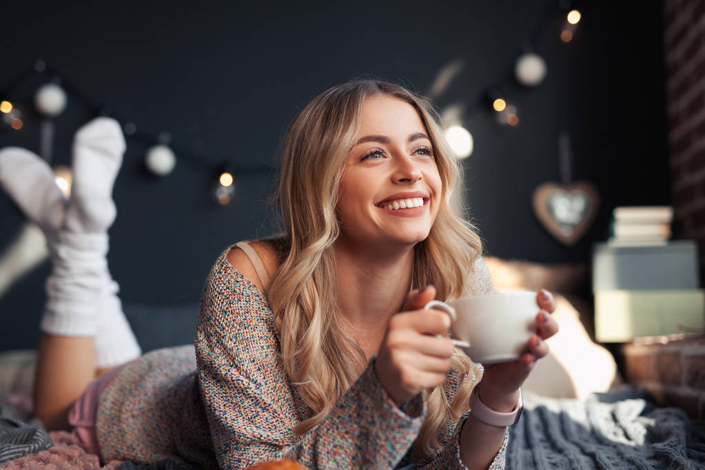 Happy woman having hot drink on bed - Photo, Image