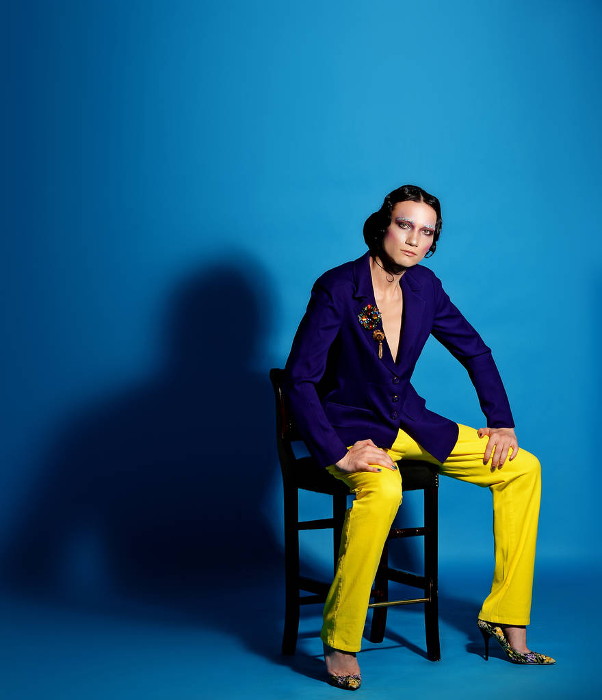 male make-up in a blue blazer and yellow pants posing on blue background - Photo, Image