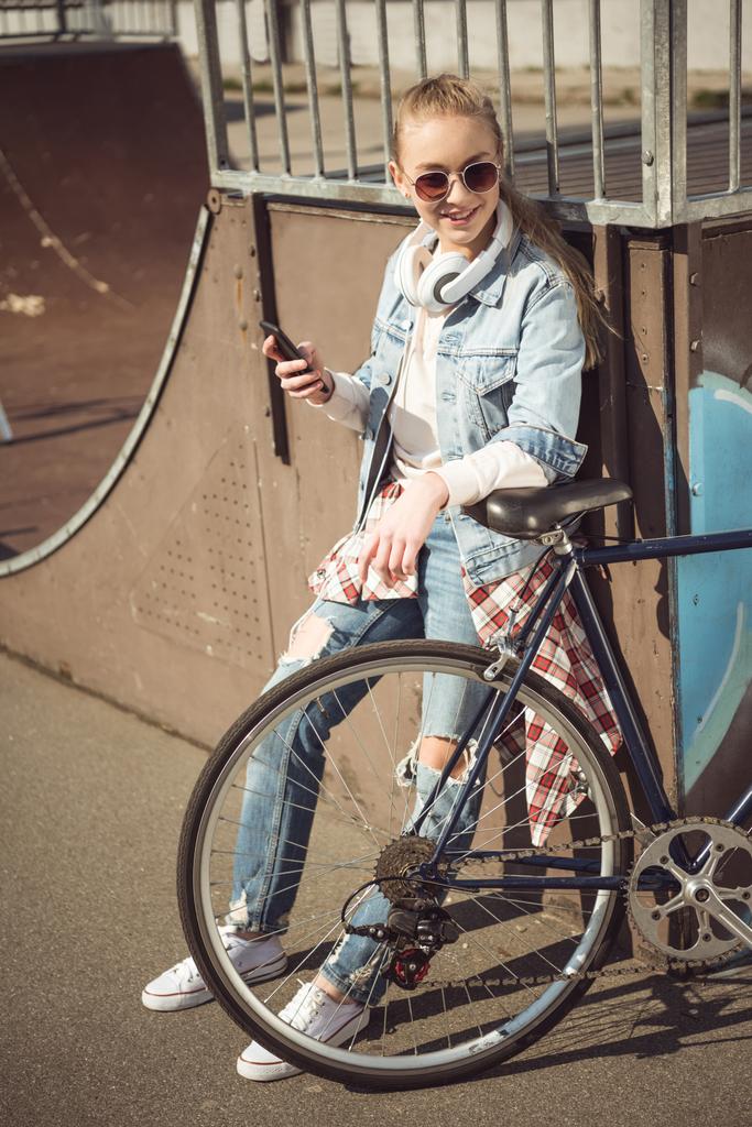 Chica con bicicleta usando teléfono inteligente
  - Foto, Imagen