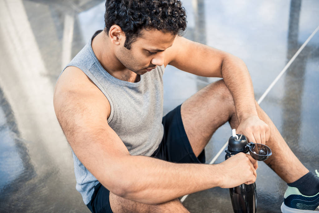 άνθρωπος με μπουκάλι νερό που αναπαύεται στο γυμναστήριο - Φωτογραφία, εικόνα