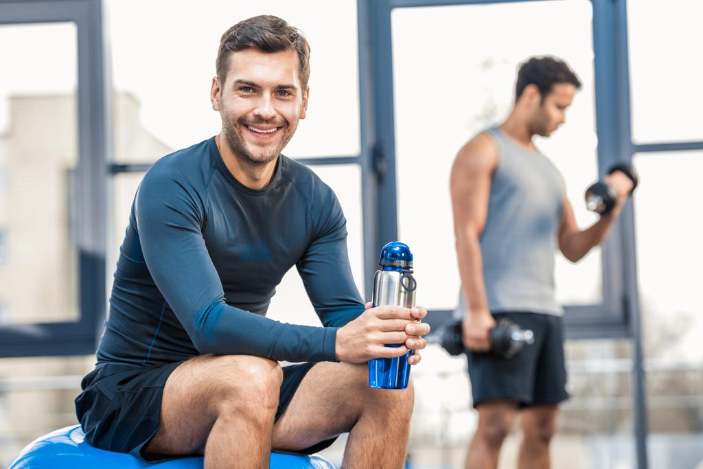 άνθρωπος με μπουκάλι νερό που αναπαύεται στο γυμναστήριο - Φωτογραφία, εικόνα