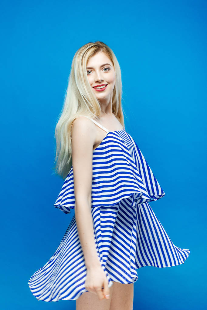 Söpö nuori nainen poseeraa studiossa. Muotokuva kaunis blondi yllään raidallinen kesä mekko sininen tausta
. - Valokuva, kuva