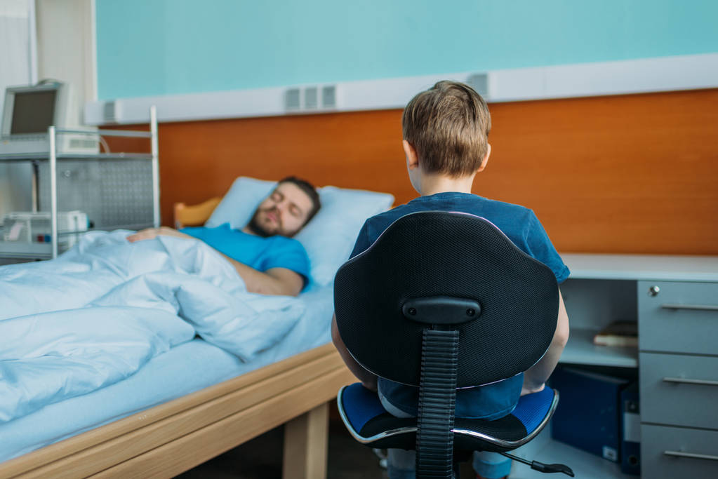 сын сидит рядом с больным отцом в отделении
 - Фото, изображение